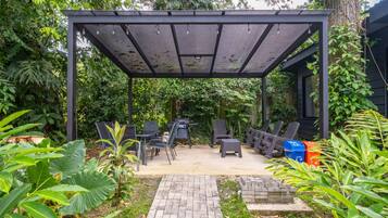 A covered patio area with outdoor furniture, a brick pathway, and lush greenery.