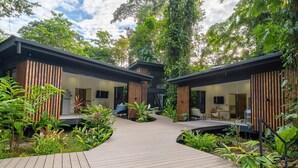 A modern outdoor area with wooden deck, seating, and lush greenery.
