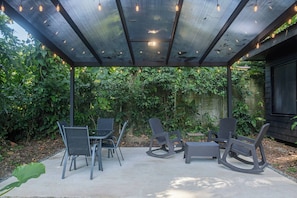 Een terras buiten met een overdekte zithoek, inclusief stoelen en een tafel.