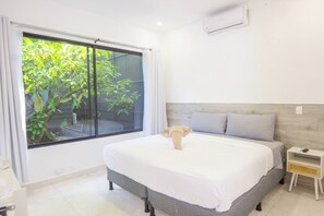 A bedroom with a large window, a bed, a nightstand, and a wall-mounted air conditioner.