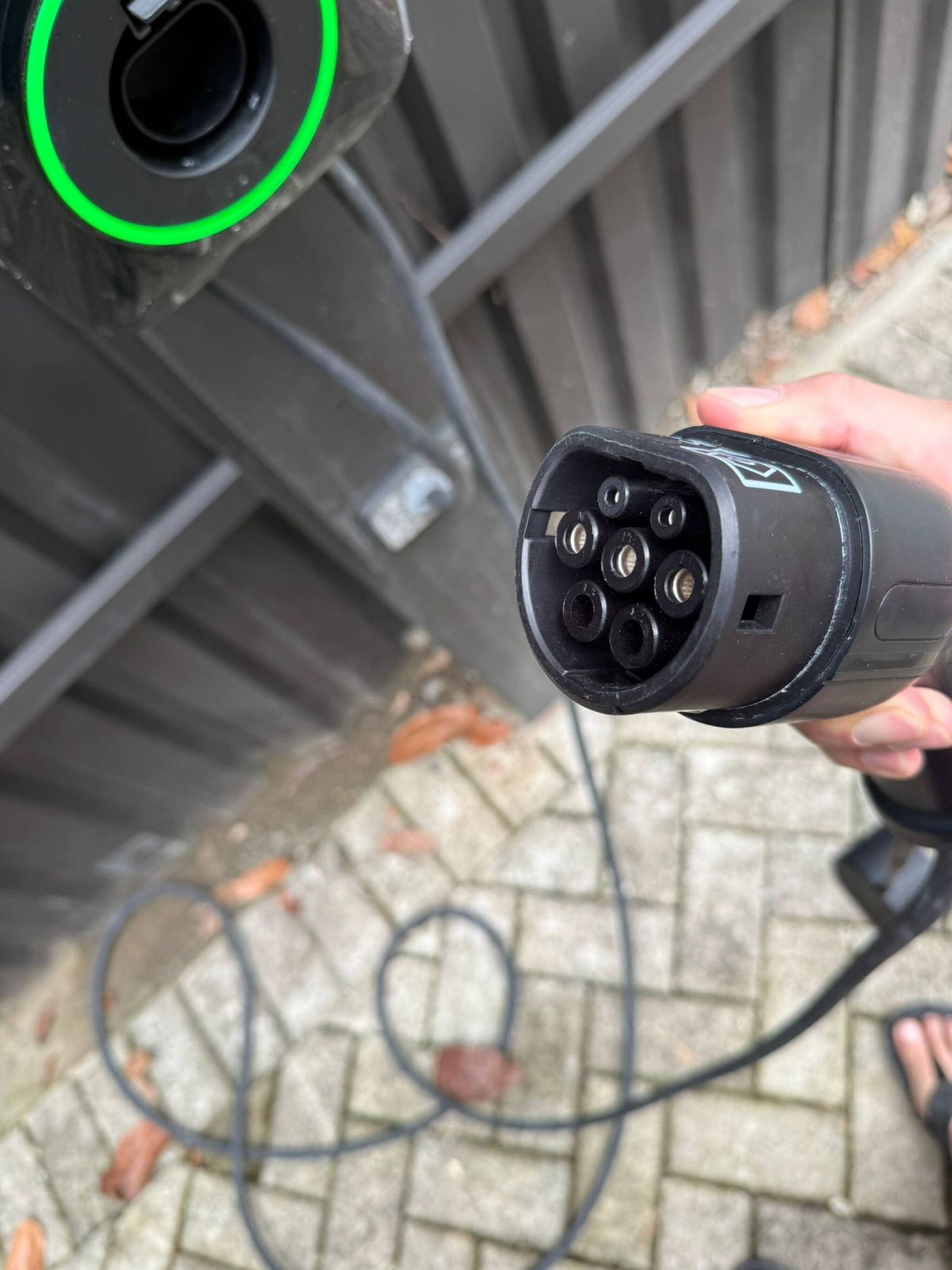 A hand holding a black power cord with multiple plugs, connected to a wall socket with a green light indicator.