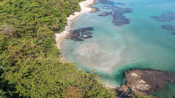 An aerial view of a coastal area with clear turquoise waters, sandy beaches, and dense green vegetation.