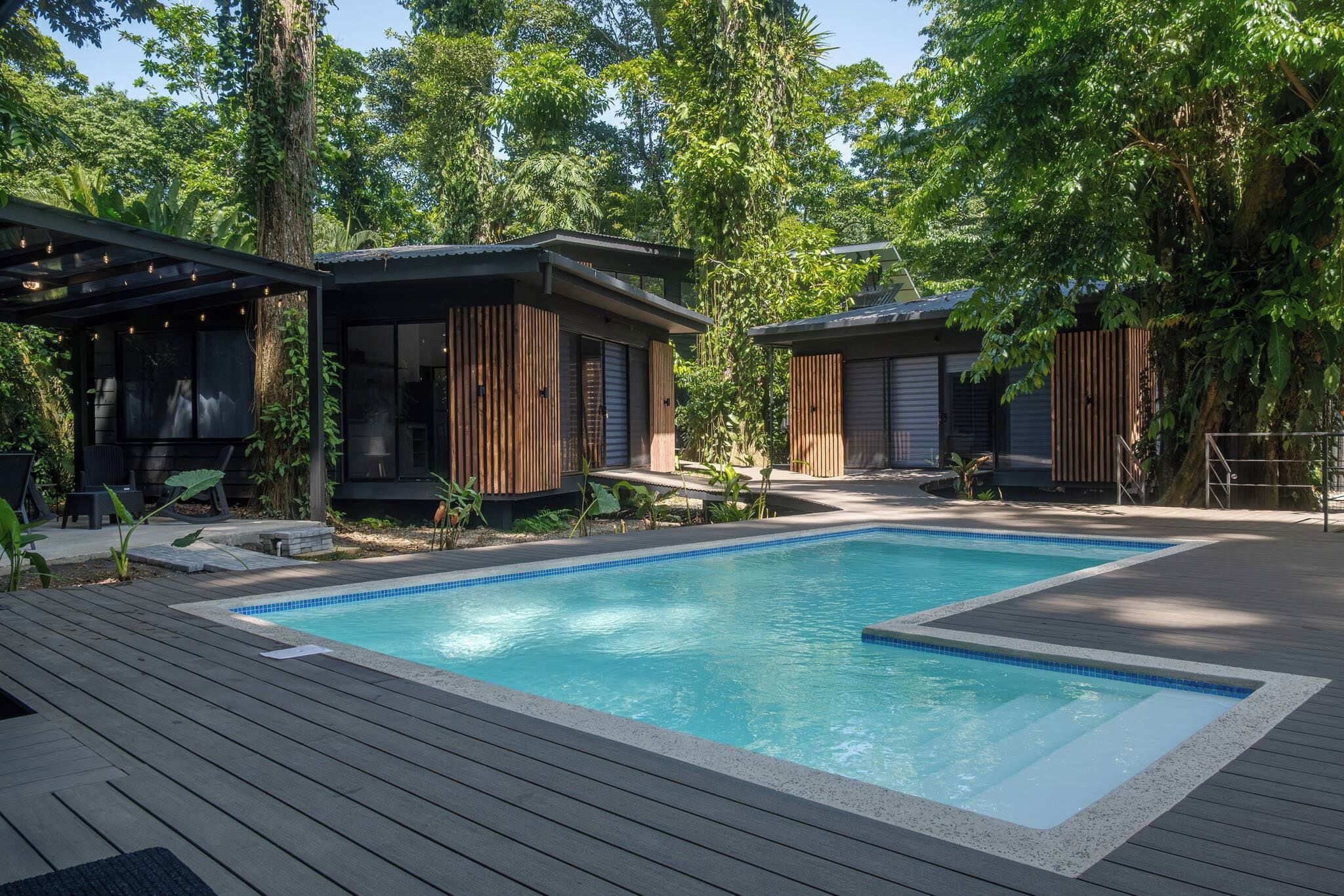 A modern outdoor pool area with wooden deck and two contemporary buildings with large windows.
