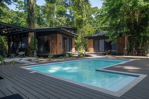A modern outdoor pool area with wooden deck and two contemporary buildings with large windows.