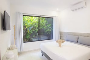 Een hotelkamer met een bed, een televisie, een raam met gordijnen en een airconditioning.