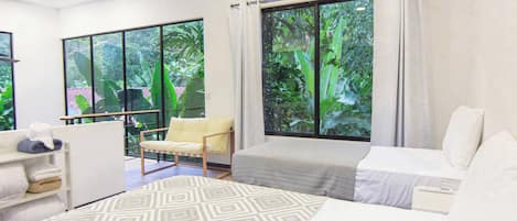 Una habitación de hotel con cama, una silla, un escritorio y ventanas grandes con cortinas.