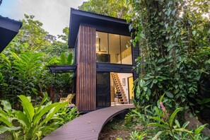 Een modern huis met twee verdiepingen, met een houten gevel, een glazen toegangsdeur en een trap naar de bovenverdieping.