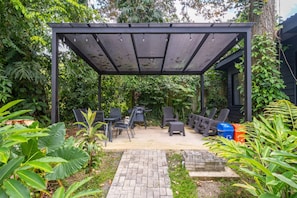 Een overdekte patio met tuinmeubilair, een met stenen bestraat pad en weelderige beplanting.