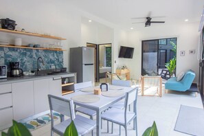 A modern kitchen with a dining area, a flat-screen TV, and a seating area with a blue chair.