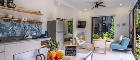 A modern kitchen with a dining area, a flat-screen TV, and a seating area with a blue sofa.