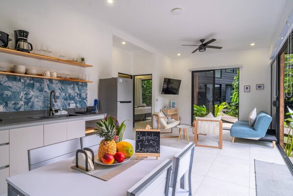 A modern kitchen with a dining area, a flat-screen TV, and a seating area with a blue sofa.