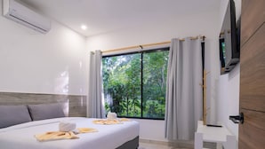 Une chambre d’hôtel avec un lit, une télévision, une fenêtre avec des rideaux et une vue sur la verdure.