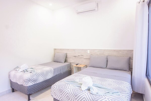 A hotel room with two beds, a wooden headboard, a nightstand, and an air conditioning unit.