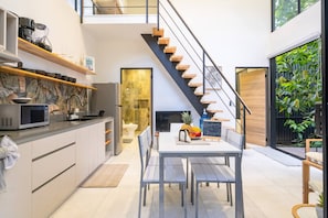 A modern kitchen with a dining area, a staircase, and a view of greenery outside.