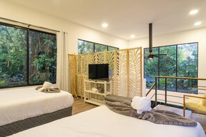 A hotel room with two beds, a TV, a wooden partition, and large windows with a forest view.