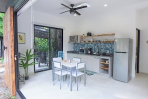 A modern kitchen with a dining area, a ceiling fan, and a view of greenery outside.