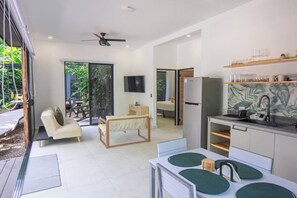A modern kitchen with a refrigerator, a dining table with chairs, and a television mounted on the wall.