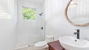 Een moderne badkamer met een douchecabine van glas, een toilet en een wastafel met een spiegel erboven.