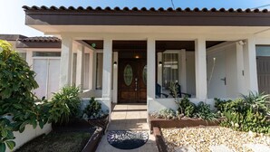 A two-story house with a covered porch, a wooden front door, and a small garden with various plants.