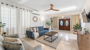A living room with a blue sofa, a coffee table, and a ceiling fan. - Multifamily 413 home near beach & plaza (Rincon)