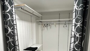 Una habitación con cama, un estante pequeño, un perchero y un radiador.