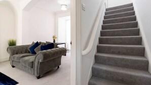 Un salon avec un canapé gris, un escalier et un intérieur blanc.
