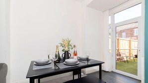 Un coin repas avec une table noire dressée pour quatre personnes, comprenant des assiettes, des verres et un vase avec des fleurs.