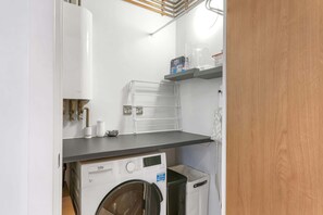 A compact laundry room with a washing machine, a dryer, and a shelf with cleaning supplies.