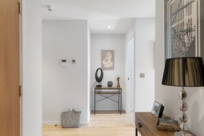 A hallway with a wooden floor, a console table with a lamp, a framed picture, and a wicker basket.