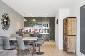 A modern kitchen with a dining area, featuring a central island, pendant lighting, and a built-in oven.