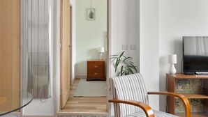 A modern living room with a wooden door, a striped armchair, a small cabinet with a television, and a plant.