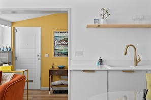 Una cocina moderna con armarios blancos, una pared de acento amarilla, una estantería de madera con adornos, y un grifo dorado.