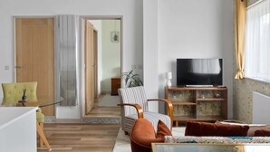 A living room with a TV, a sofa, a striped chair, and a wooden cabinet.