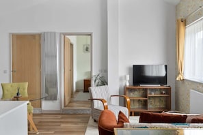 Una sala de estar con televisor, sofá, una silla a rayas y un mueble de madera.