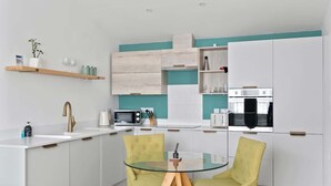A modern kitchen with white cabinets, a glass dining table, and yellow chairs.