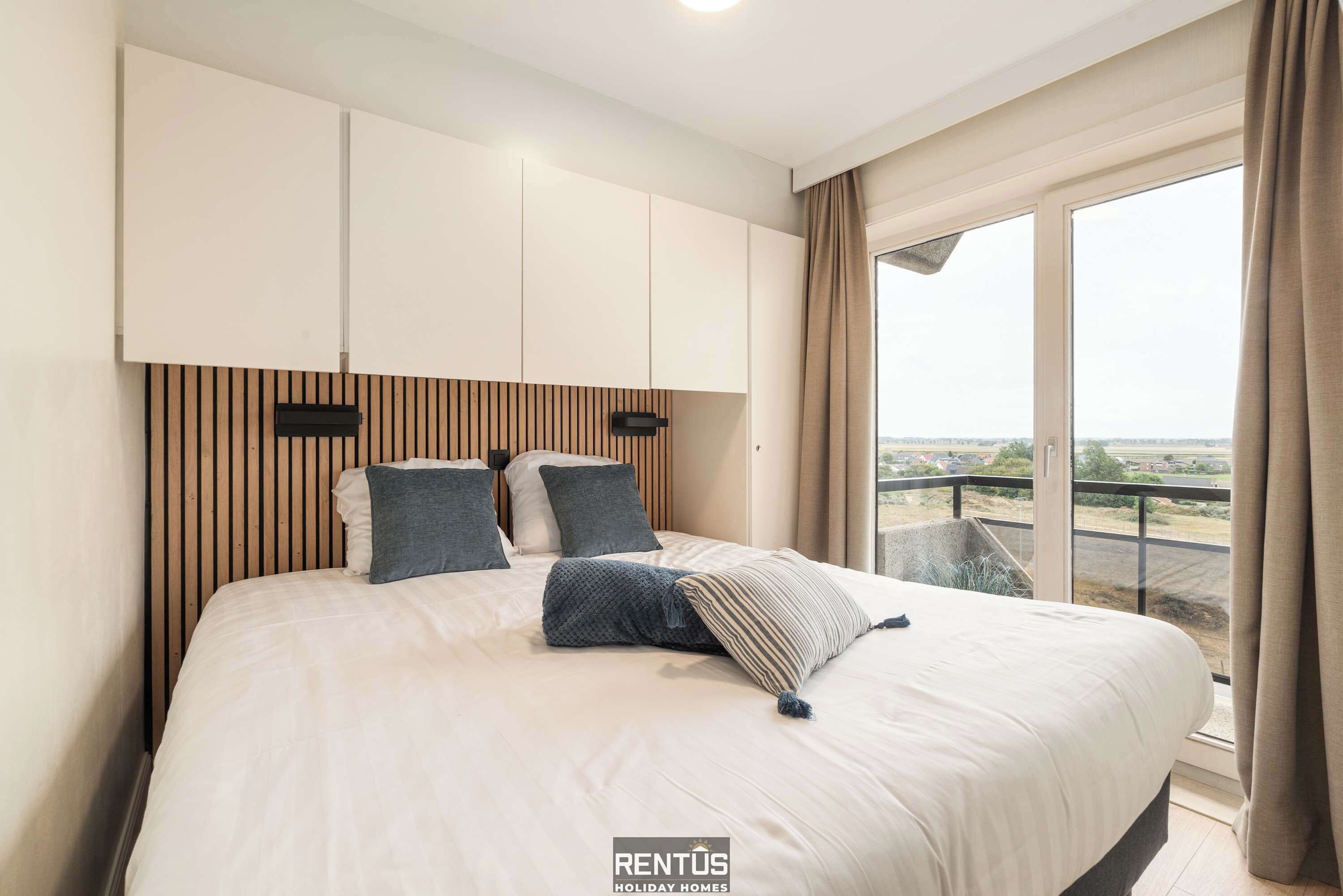 A bedroom with a large bed, a wooden headboard, and a view of the outside through a large window.
