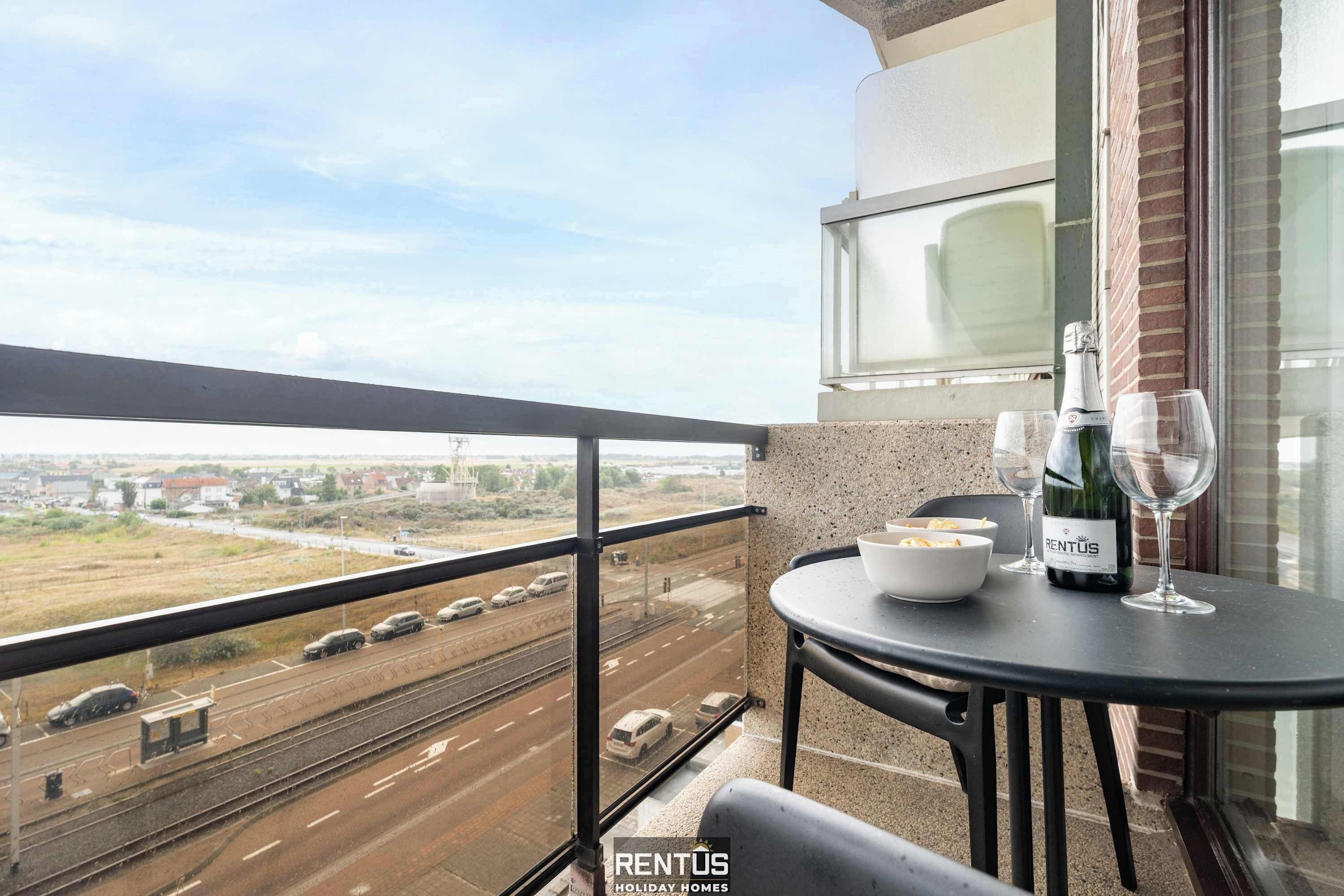 A balcony with a table, a bottle of wine, and a bowl of chips.