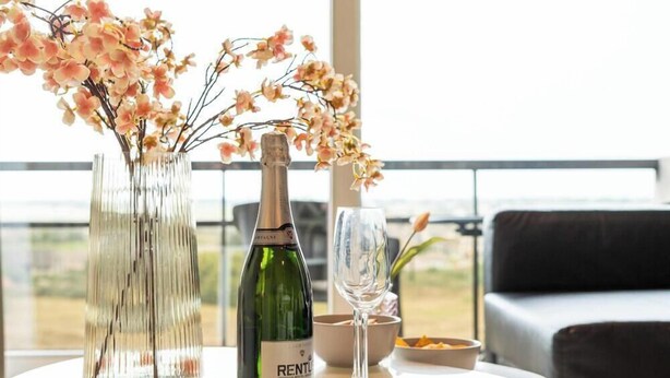 A table with a bottle of wine, a glass, and a vase with flowers.