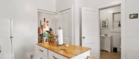 Una cocina con armarios blancos, encimera de madera y una puerta que da a un baño.
