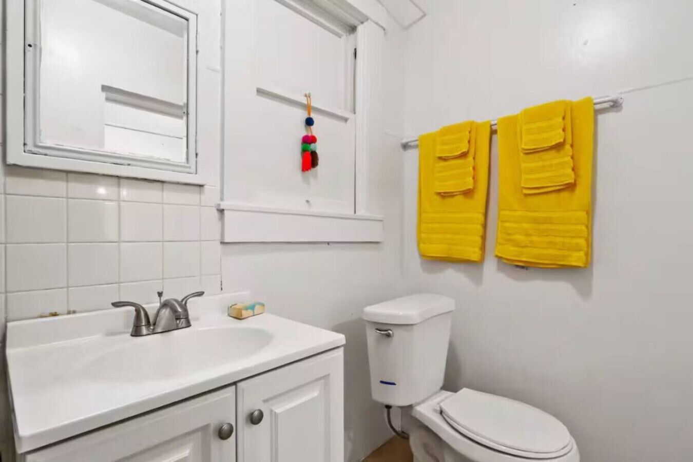 A bathroom with a white sink, mirror, toilet, and two yellow towels on a rack.
