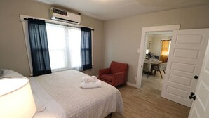 Una habitación de hotel con cama, una silla, una puerta y un equipo de aire acondicionado.