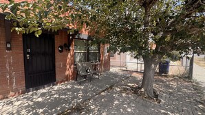 Un edificio de ladrillo con una puerta negra, un banco y un árbol en la parte delantera.