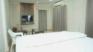 Habitación de hotel con cama, escritorio, silla, televisor y aire acondicionado.