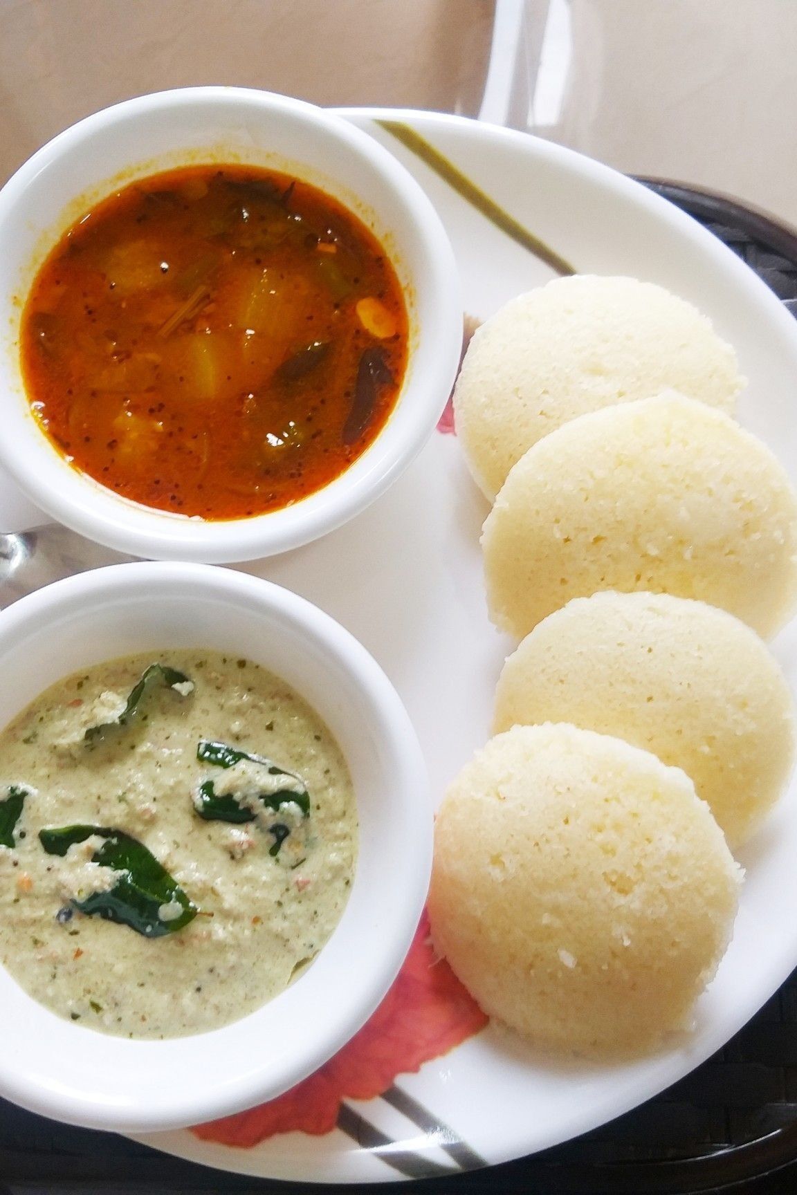Een bord met drie witte idli's en twee kleine schaaltjes met chutney.
