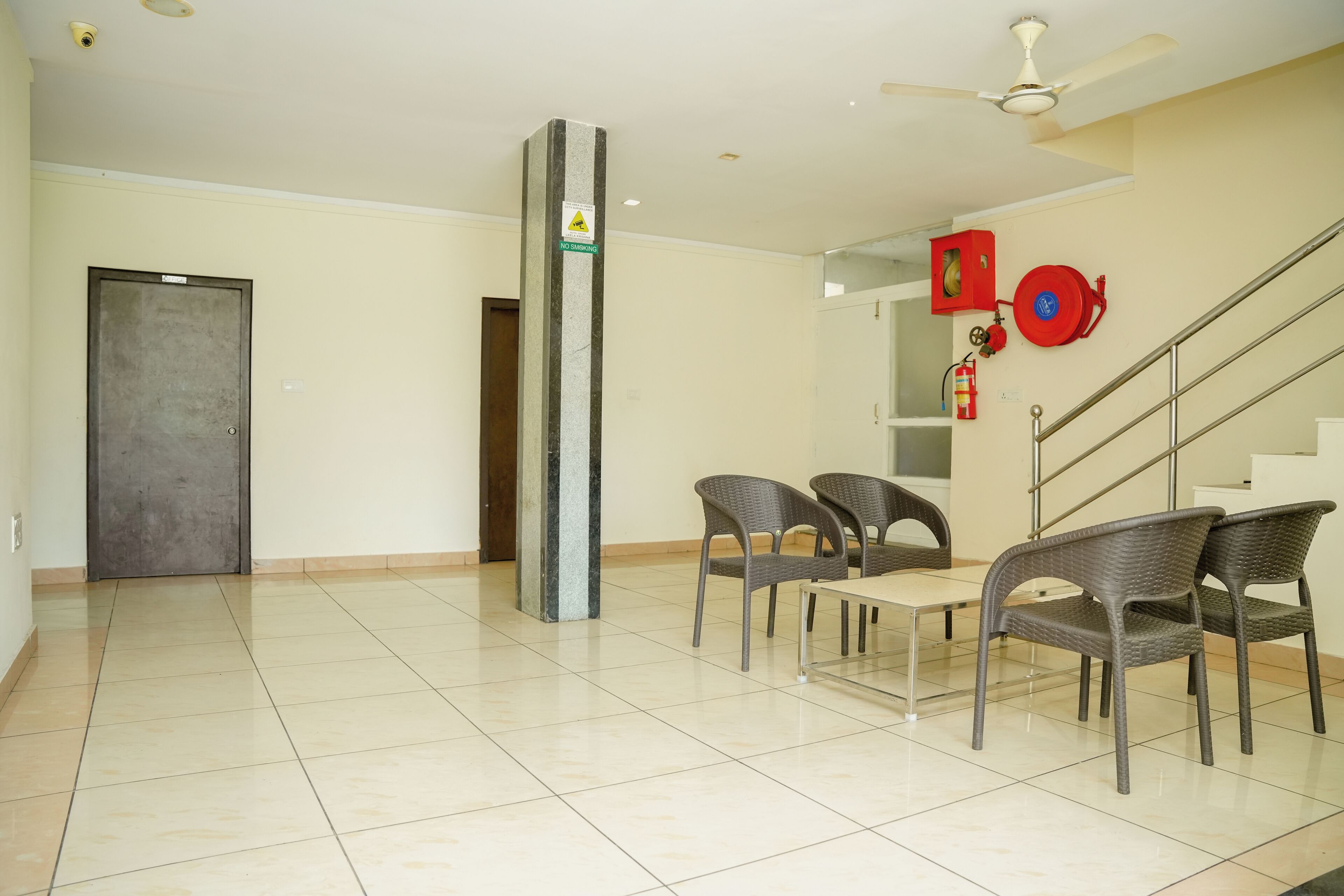 A spacious room with a tiled floor, a ceiling fan, a fire extinguisher, and a staircase.