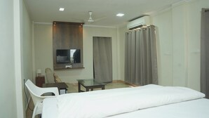 A hotel room with a bed, a desk, a chair, a television, and a ceiling fan. - Hotel Grand Leela Krishna  (Bhimavaram)