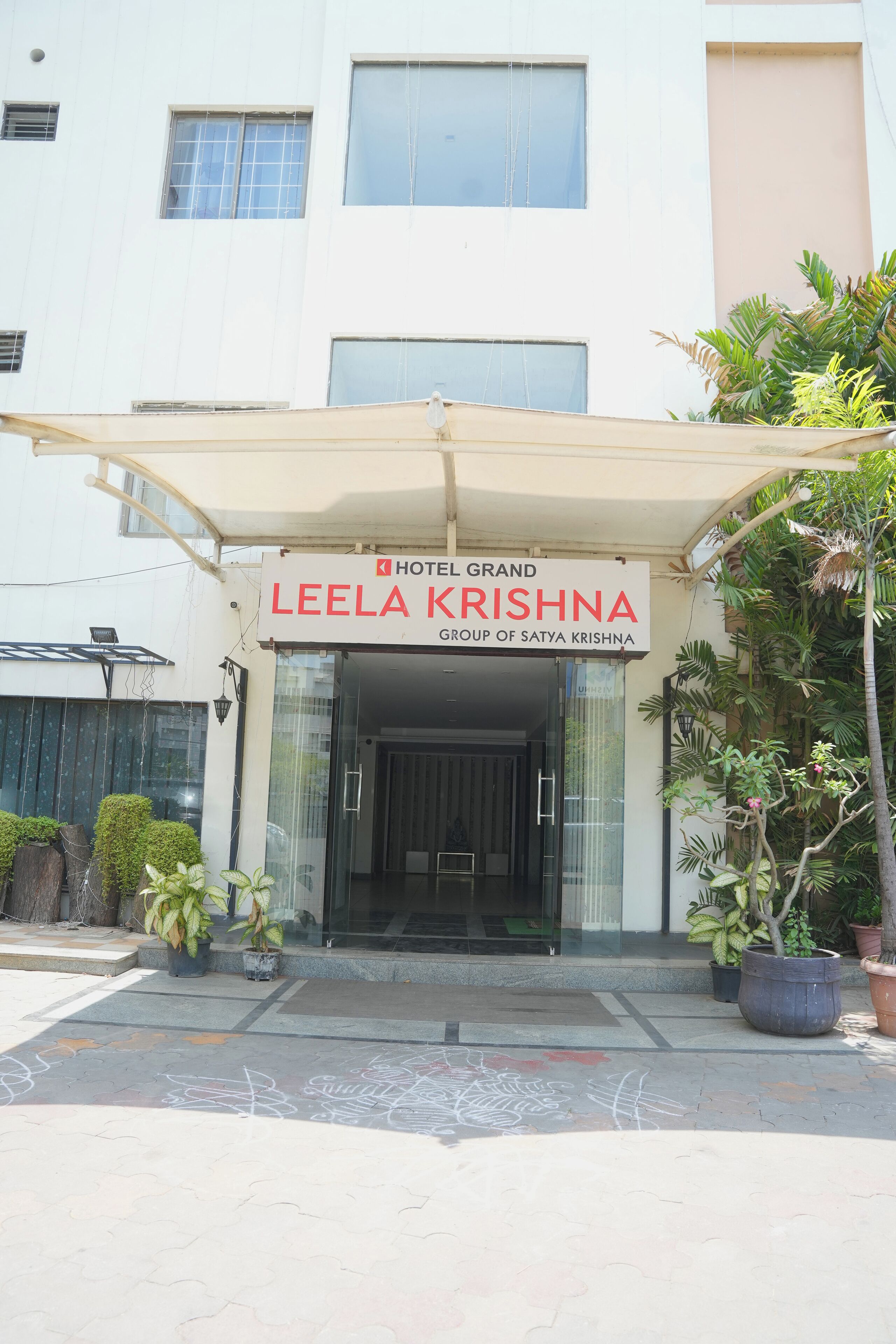 The entrance of Hotel Grand Leela Krishna with a clear signboard, a covered entrance, and potted plants around.