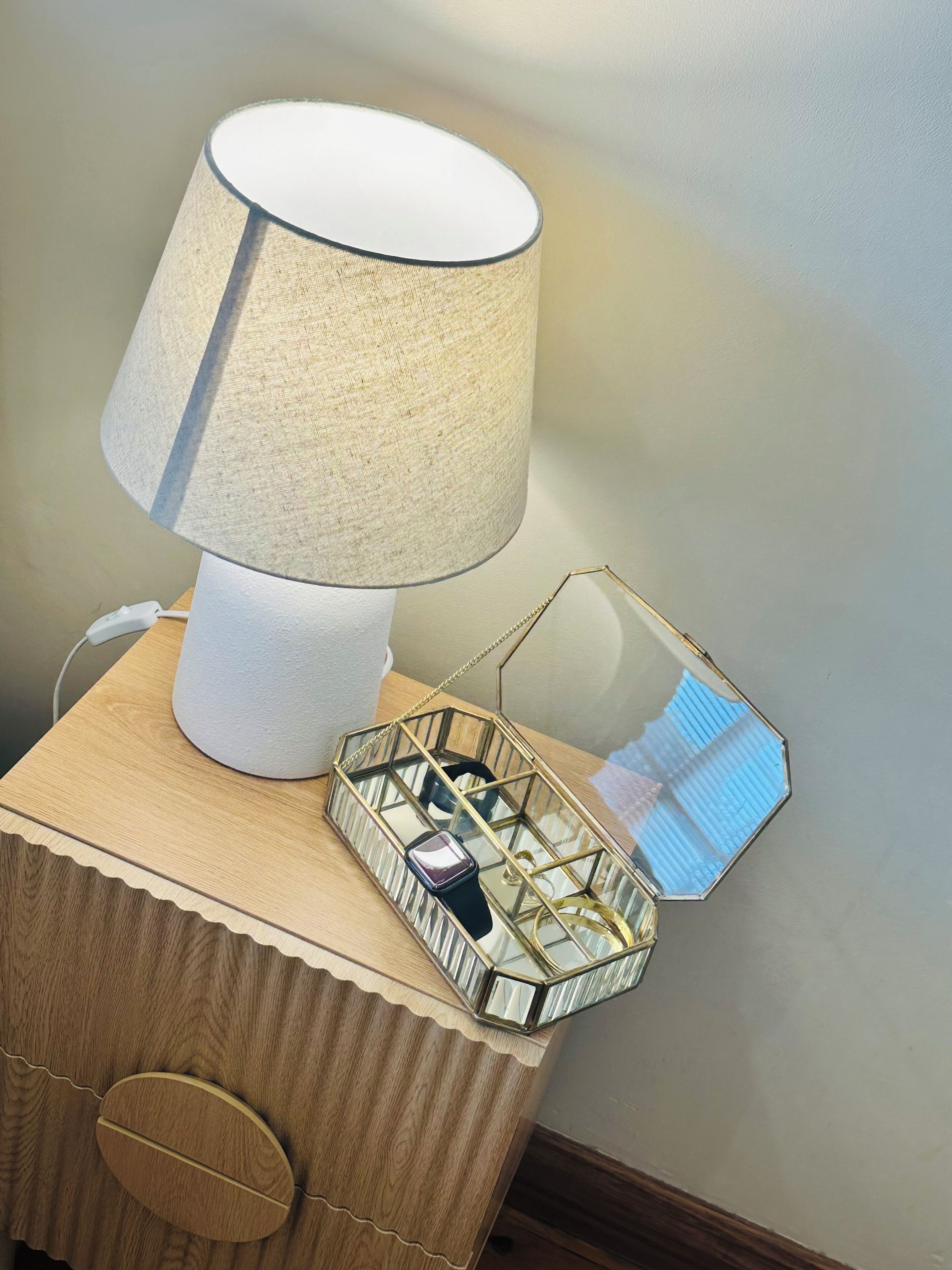A bedside table with a lamp, a geometric glass container, and a power cord.