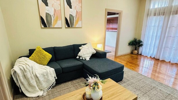 A modern living room with a dark-colored sofa, a wooden coffee table with decorative items, and a large window with sheer curtains.