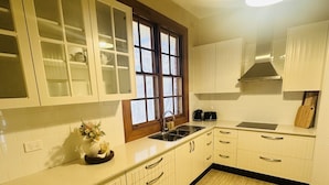 A kitchen with white cabinets, a wooden countertop, a window with blinds, and a light fixture.